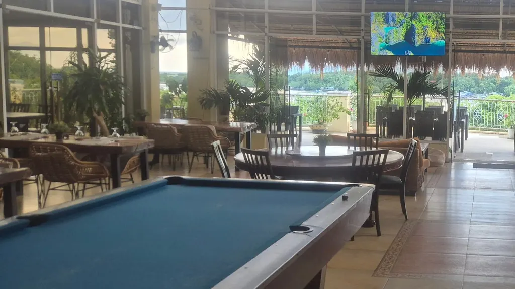 The restaurant floor: a pool table, wooden tables laid for dinner, and the water through tall windows.